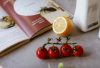Flat lay of cooking ingredients including tomatoes and a lemon with a cookbook.
