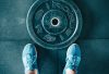 Blue sneakers next to a weight plate on a gym floor, top view.