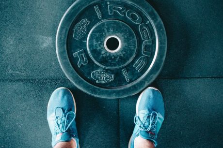 Blue sneakers next to a weight plate on a gym floor, top view.