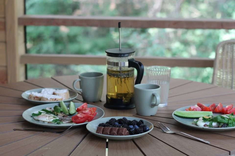 Casual breakfast with berries, veggies, and tea on a wooden porch table.